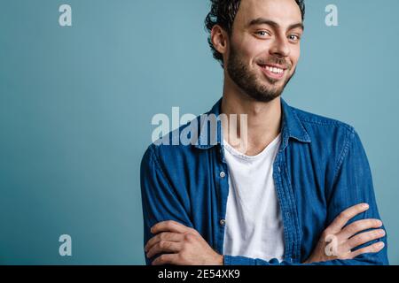 Joyful handsome guy smiling and while posing with hands crossed isolated over blue background Stock Photo