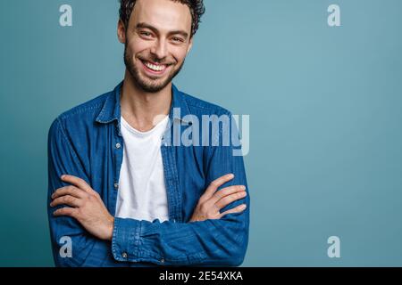 Joyful handsome guy smiling and while posing with hands crossed isolated over blue background Stock Photo