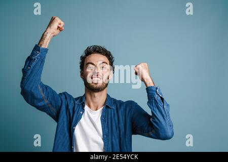 Happy young man celebrating success over blue background, looking at camera Stock Photo