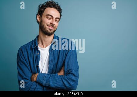Joyful handsome guy smiling and while posing with hands crossed isolated over blue background Stock Photo