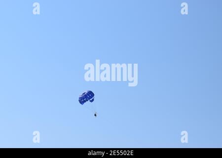 Recreational parakiting background - silhouetes of three people under blue parachuting canopy towed behind a boat. Parasailing trio in the sky above t Stock Photo