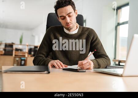 Entrepreneur working with a laptop and documents in an office, taking notes Stock Photo