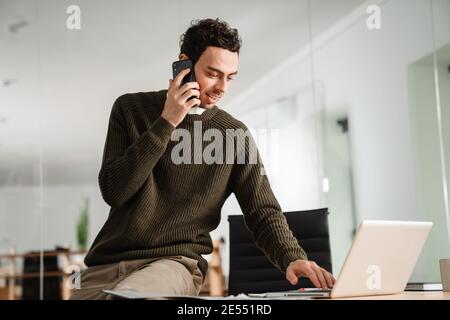 Confident young manager working at the office, holding documents, using laptop computer Stock Photo