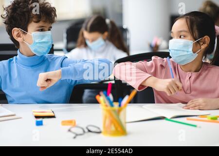 Diverse pupils wearing face masks greeting and bumping elbows Stock Photo