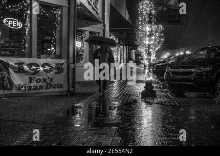Prattville, Alabama/USA - December 20, 2018: Woman walks along a festively lit sidewalk in front of Fox's Pizza on Main Street on a rainy night. Stock Photo