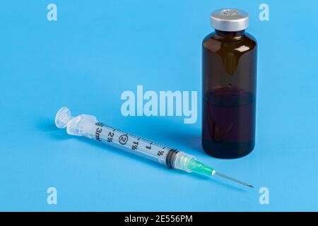 A close-up shot of a hygienic single-use plastic disposable syringe injection with amber color vial set on blue background. Stock Photo