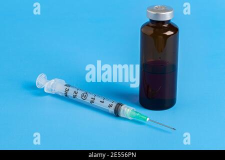 A close-up shot of a hygienic single-use plastic disposable syringe injection with amber color vial set on blue background. Stock Photo