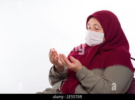 Old Turkish woman wearing a mask prays Stock Photo