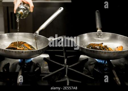 Chef hand while pouring wine on the pans cooking lobsters on the stove Stock Photo