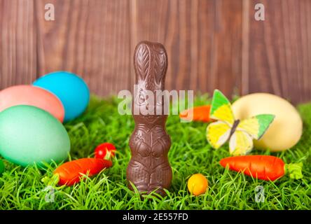 Easter colorful eggs, chocolate bunny, carrots candy in the grass on the wooden background. Stock Photo
