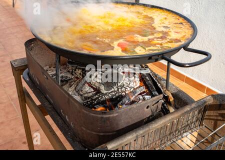 Valencian Paella being cooked on a barbecue with lots of fine oak wood. Spanish typical food. Selective focus. Healthy food concept Stock Photo