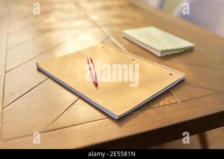 Top view of brown wooden table with notebook in recycled cover on spiral with pen and book Stock Photo