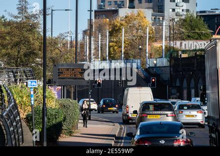 Essential travel only electronic sign on the dual carriageway running past university building train station with heavy traffic and lay walking alone Stock Photo