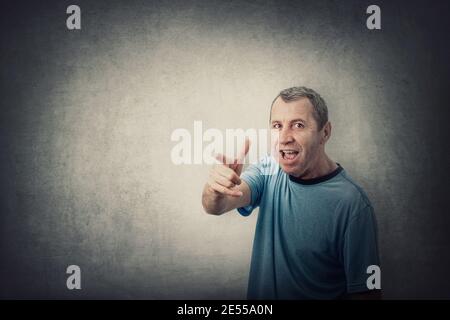 Angry middle aged man pointing index finger screaming, like scolding someone, isolated on grey wall background with copy space. Irritated and annoyed Stock Photo