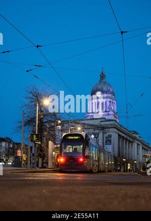 Council house illuminated with tram parked in front lit up night street lamps cables train waiting passengers shoppers to board blue sky Nottingham Stock Photo