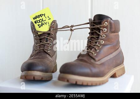 Pair of boots with laces tied together with a note with the phrase Happy Fool's Day. Stock Photo