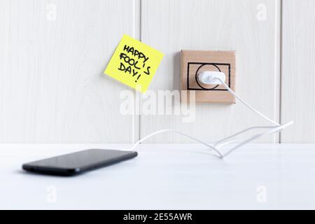 Mobile phone connected to a cardboard plug next to a sticky note with the phrase 'Happy fool's day'. Space for text. Stock Photo