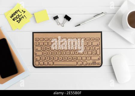Cardboard computer keyboard on office desk. Nearby are sticky notes with the phrase 'Happy fool's day'. Stock Photo