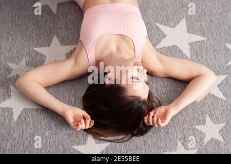 close - up upside-down portrait of a young woman in a pink sports top lying on a gray carpet with white stars Stock Photo