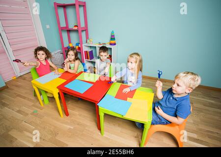 Children show scissors and get ready to cut colored cardboard Stock Photo