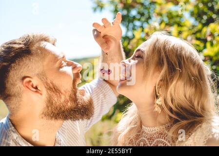 Happy couple spend time together and feed each other cherries in summer outdoors Stock Photo