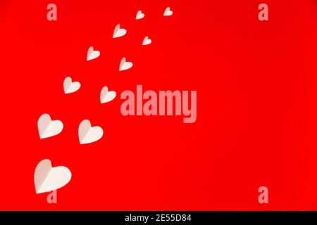 White paper hearts over the red background in flat lay style. Valentine's Day composition. Holiday concept Stock Photo