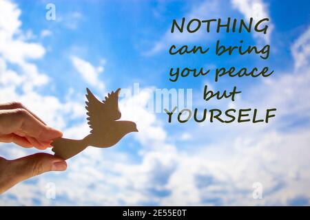 Man hand holding wooden bird on cloud sky background. Words 'nothing can bring you peace but yourself'. The development of the imagination, copy space Stock Photo