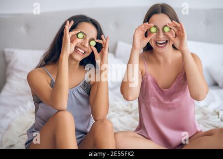 Two cute young girls with slices of cucumber in hands Stock Photo
