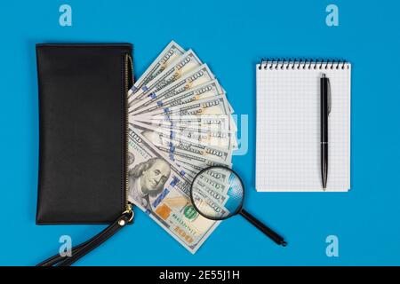 100 US dollars bills and magnifying glass with black purse and notepad. Concept of counterfeit money Stock Photo