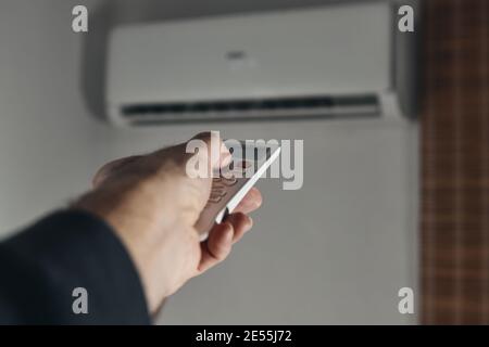 A man's hand operating the air conditioner with a remote control Stock Photo