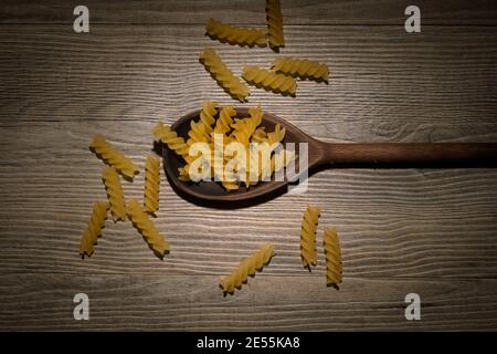 Wooden spoon with dried fusilli pasta swirls on a wooden table. Stock Photo