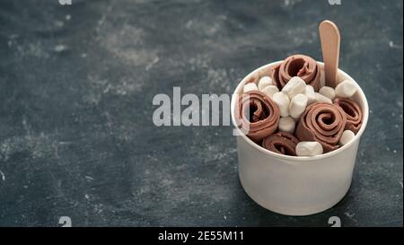 Rolled ice cream with in cone cup on dark rustic background. Iced rolls with chocolate. Thai style chocolate rolled ice cream with copy space for text or design. Banner. Natural daylight Stock Photo