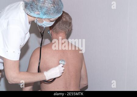 doctor listens with a stethoscope to the lungs of an elderly man from the back. Health check before coronavirus vaccination. Stock Photo