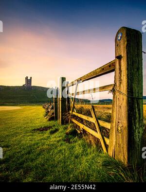 Dunstanburgh castle in Northumberland viewed through a field gate. Stock Photo