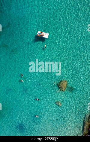An aerial shot of a beach in Greece with teenagers paddling on a water bike. Stock Photo