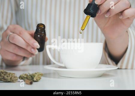 Close-up of female hand holding pipette with cbd oil, dripping into coffee mugs. Concepts of alternative medicine, natural pain reliever and herbs Stock Photo