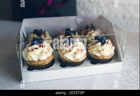 A girl cook in a gray apron packs cupcakes with cream in a gift box to send the order to the customer. Stock Photo