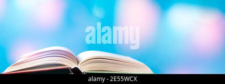 Opened old hardback book on a bright blue background with bokeh. Back to school. Space for text, banner photo. Stock Photo