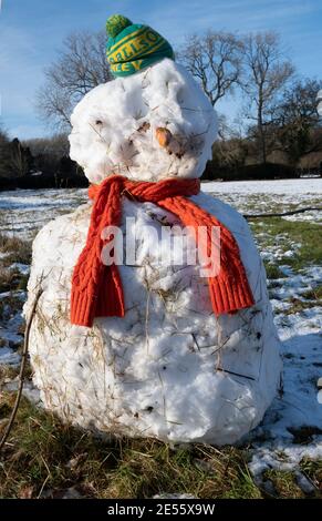Winter scene of a  snowman  on a village green , Oxfordshire ,  wearing a football supporters beany Stock Photo