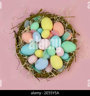 Multi-colored Easter eggs and feathers in pastel colors lie in a nest of branches on a pink background. Festive Easter card. Stock Photo