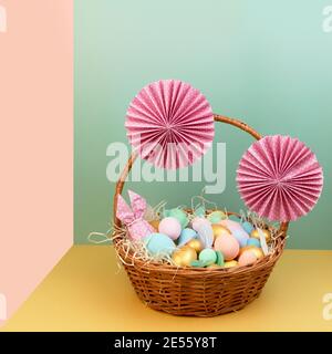 Wicker basket with colorful Easter eggs in pastel colors and decorated with paper flowers. Stock Photo