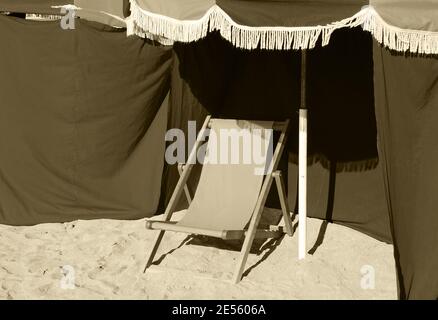 Beach wooden chaise lounge and umbrella with fringe. Trouville-sur-Mer (Normandy, France). Aged photo. Sepia. Stock Photo