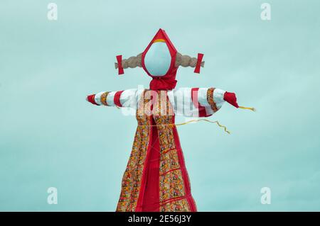 Big traditional doll against blue sky with clouds during Shrovetide in Russia. Scarecrow symbol of winter end. Stock Photo