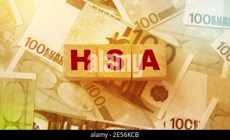 Wooden blocks with the word HSA standing for Health savings account put on 100 Euro bills. Healthcare, life insurance, medical expenses concept. Stock Photo