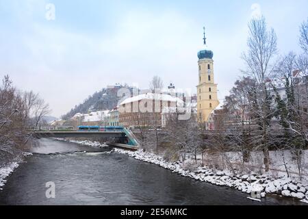 Graz, Austria-December 03, 2020: Mur river, Franciscan Church tower and famous clock tower in the background,Styria region,Austria,with snow in winter Stock Photo