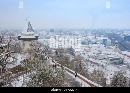 Graz, Austria-December 03, 2020: The famous clock tower on Schlossberg hill and historic buildings rooftops with snow, in Graz, Styria region, Austria Stock Photo