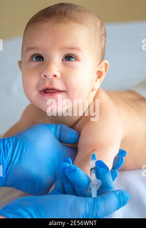 A doctor giving a vaccine to a baby in the hand. The child looks at the doctor and smiles. Vertical image Stock Photo