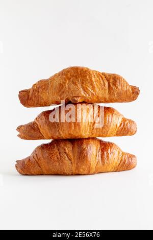 Three freshly baked croissants stacked on top of each other on a white background, vertical, close up Stock Photo