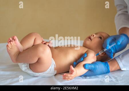 Pediatrician giving vaccine to baby lying on his back. The child looks at the doctor with interest Stock Photo