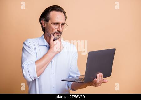 Photo of serious calm guy hold laptop finger chin look screen wear glasses shirt isolated beige color background Stock Photo